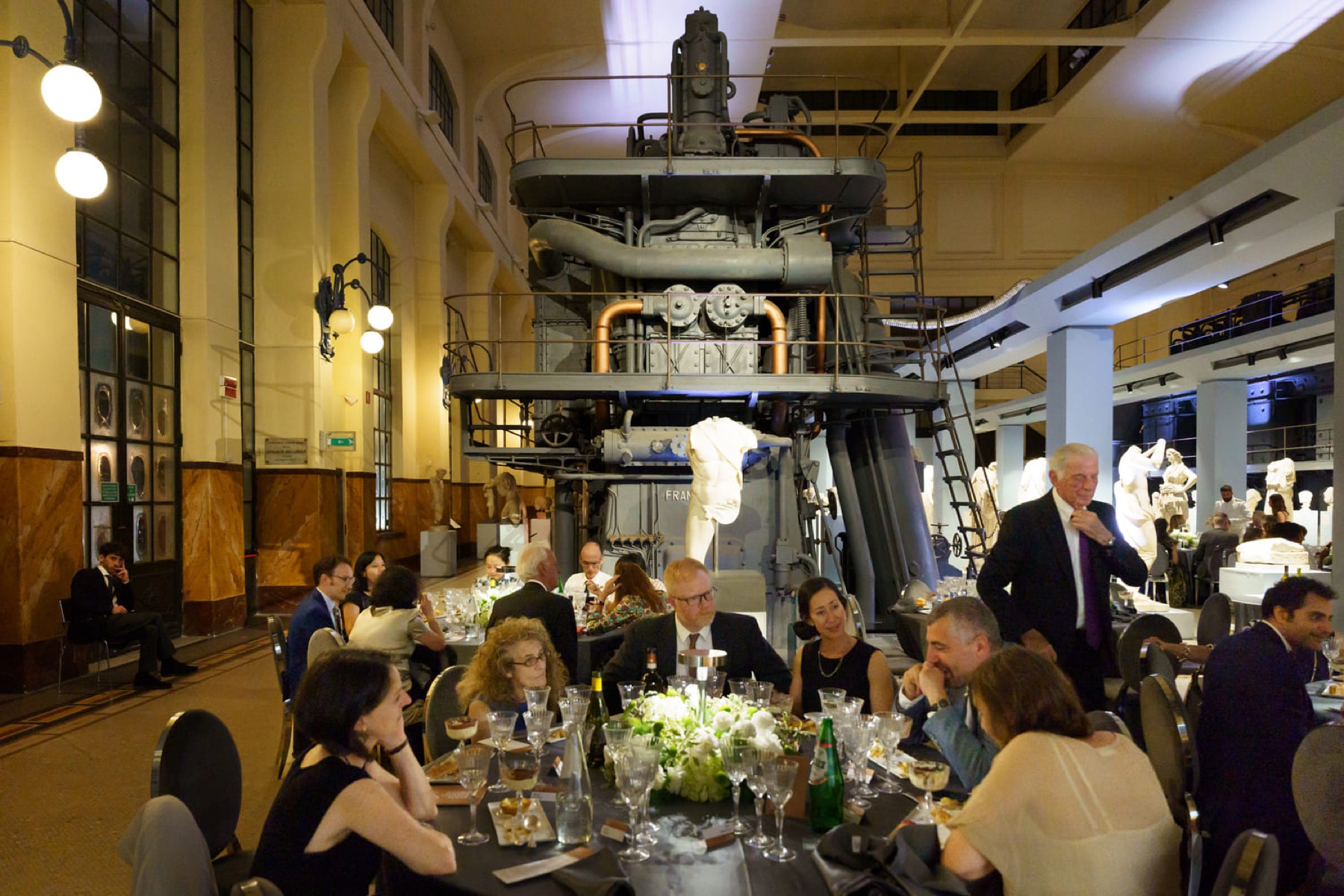 The prize dinner, guests at round tables beneath a preserved industrial engine and classical statues