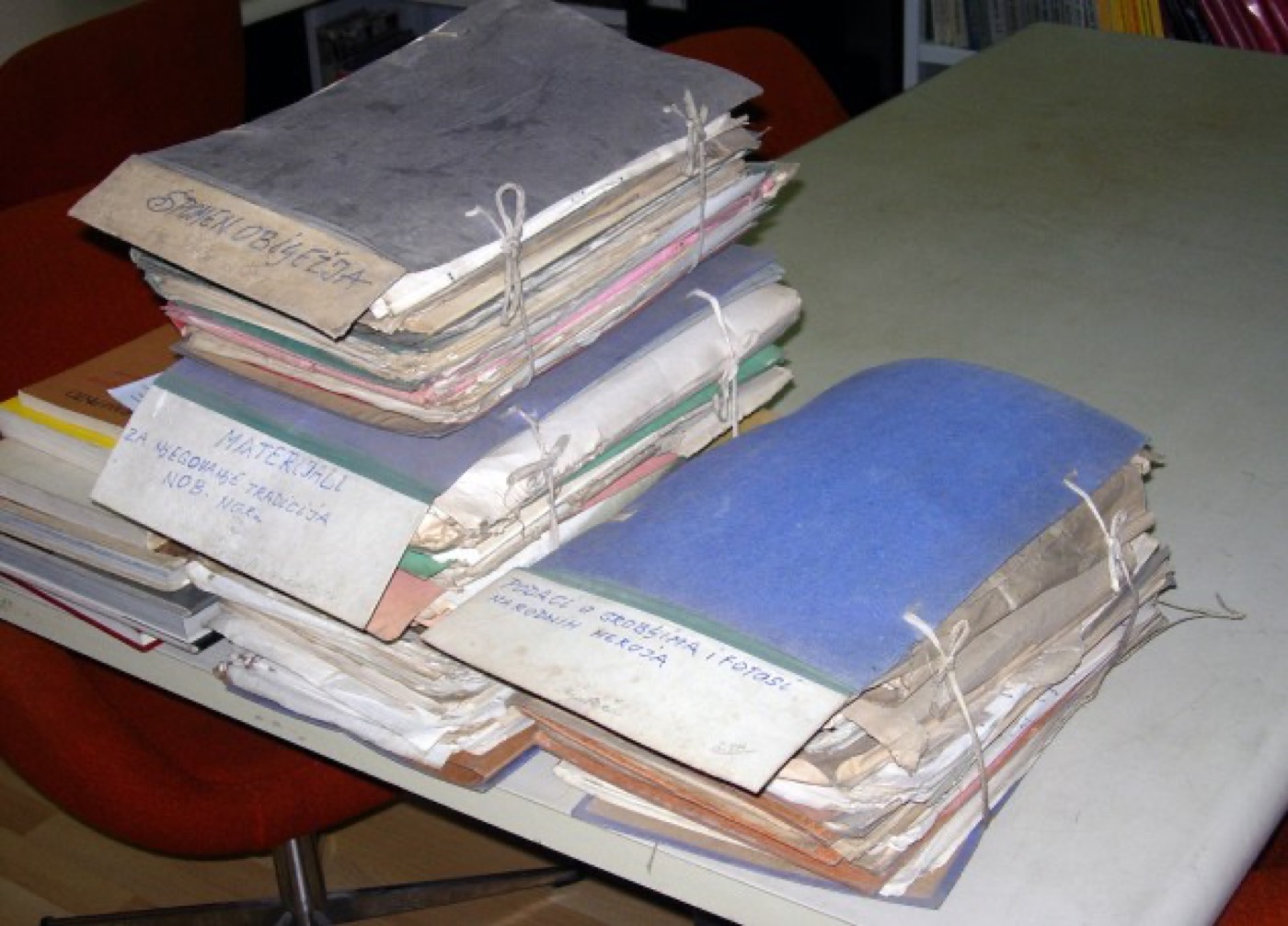 Photograph of bundled archive folders on a table, one wrapped in blue paper, titles handwritten in Serbo-Croatian