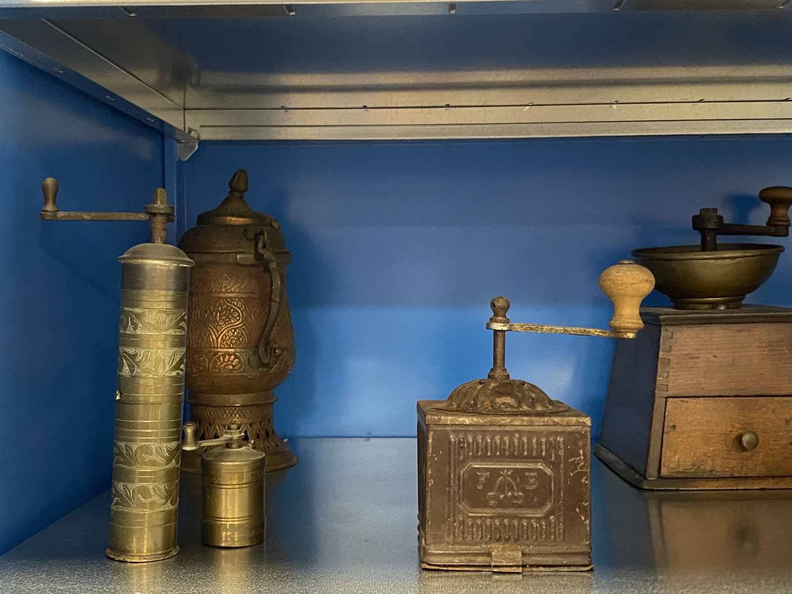 Photograph of brass coffee mills and a wooden box grinder on a blue museum shelf