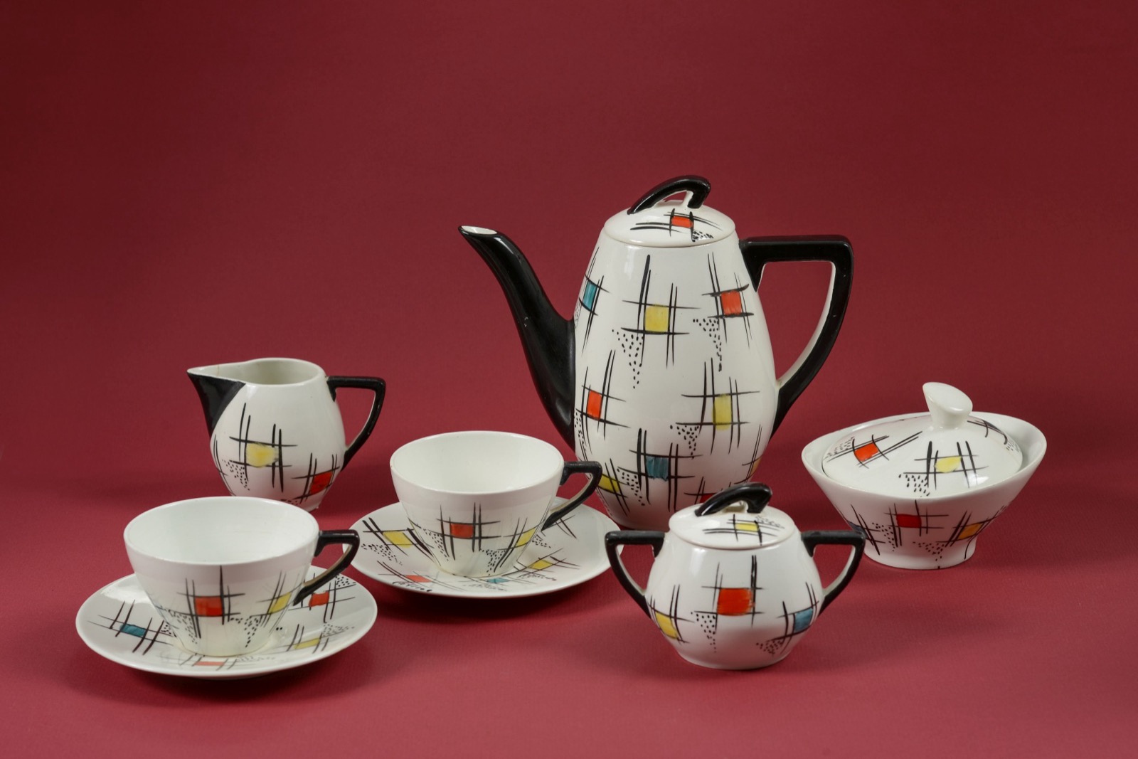 A mid-century porcelain coffee service painted with a grid of black lines and blocks of red, yellow and teal